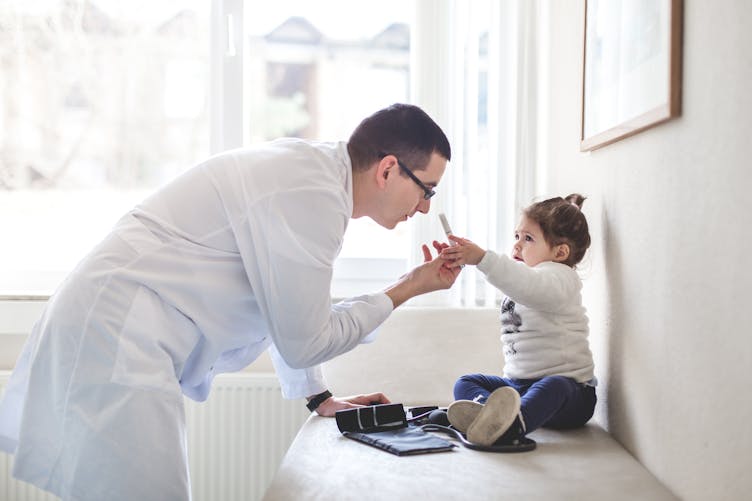 Un médecin en blouse blanche montre à une petite fille un appareil pour observer la rétine