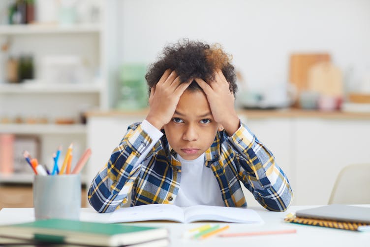 Un enfant se prend la tête dans les mains devant ses devoirs.