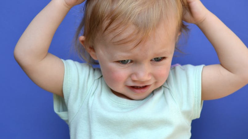Un enfant se gratte la tête et les cheveux. 