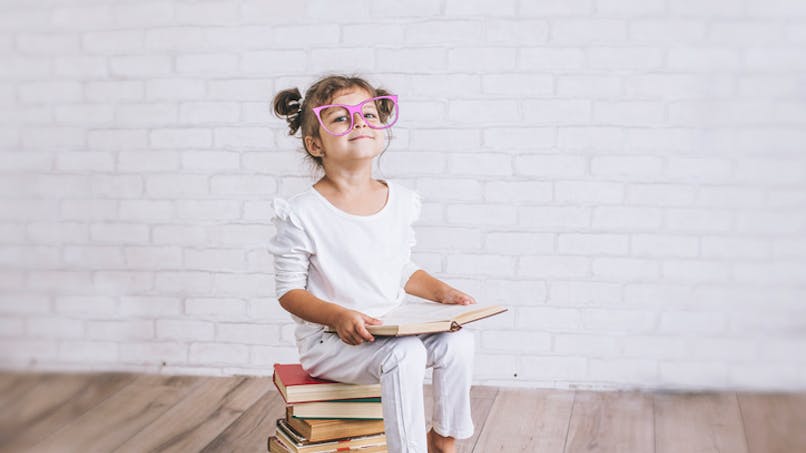 petite fille assise sur un tas de livres