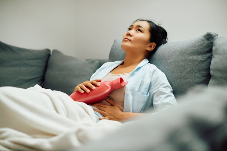 Une femme atteinte d'endométriose, dans son canapé avec sa bouillotte