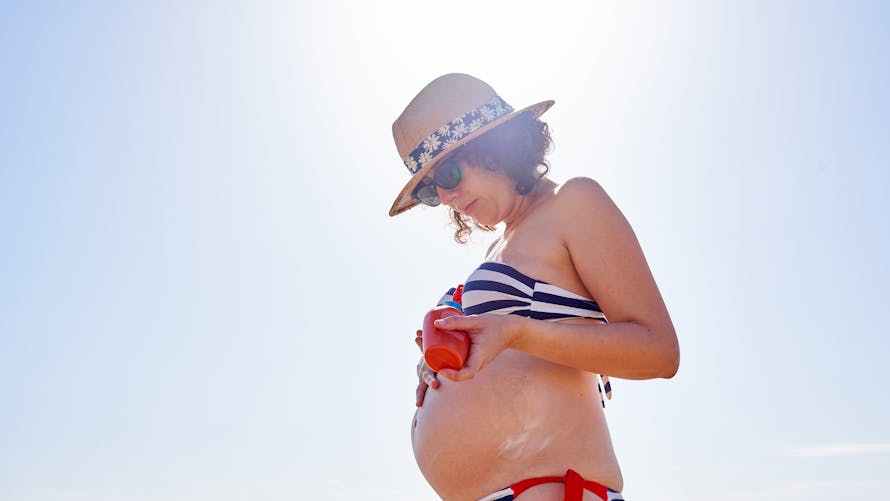 Une femme enceinte en maillot de bain se met de la crème solaire.