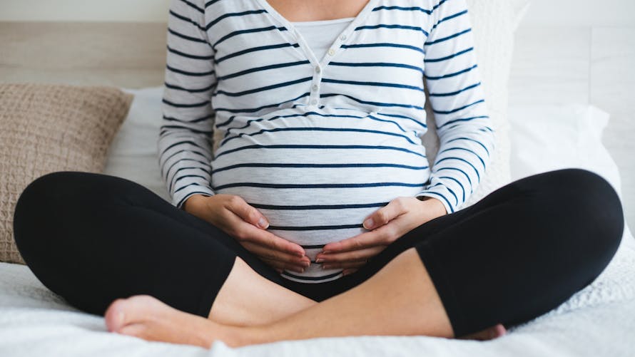 Femme enceinte assise en tailleur, tenant son ventre avec ses mains.