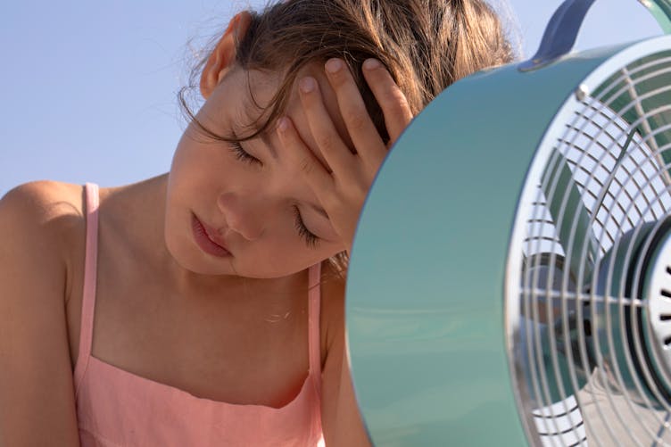 Une jeune fille devant un ventilateur allumé. 
