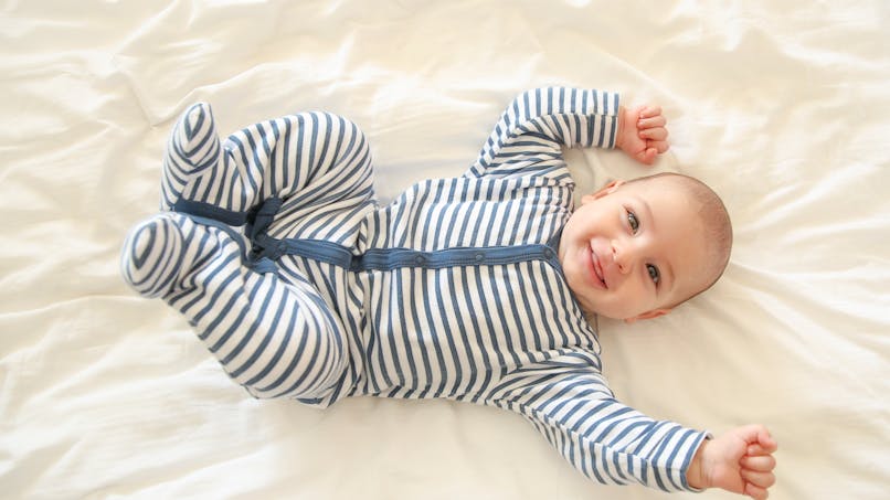 bébé souriant sur le dos, pyjama rayé bleu