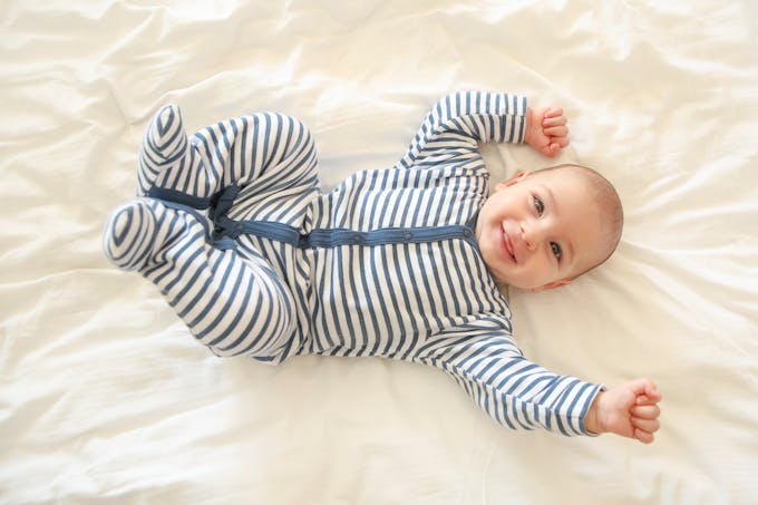 bébé souriant sur le dos, pyjama rayé bleu