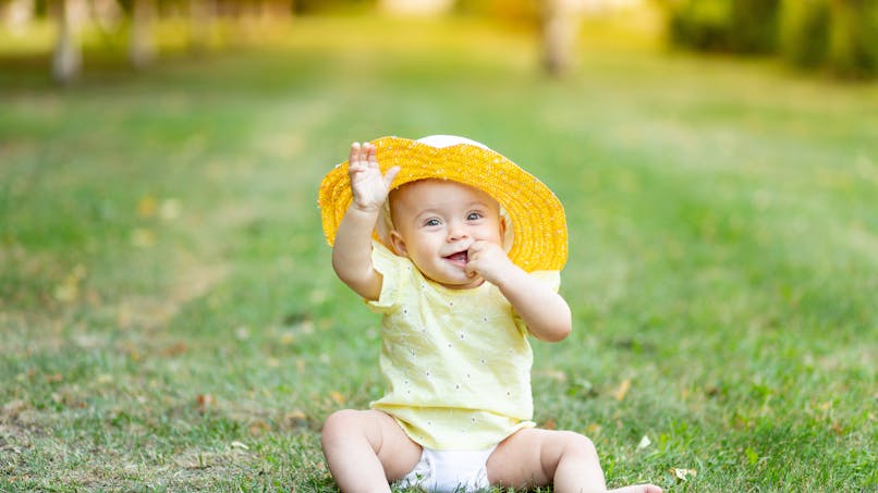 bébé assis dans l'herbe, chapeau jaune