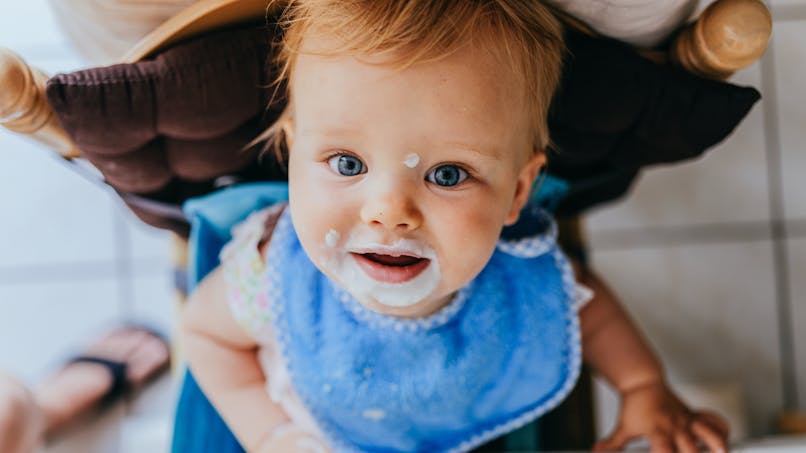 bébé dans chaise haute, bouche couverte de yaourt