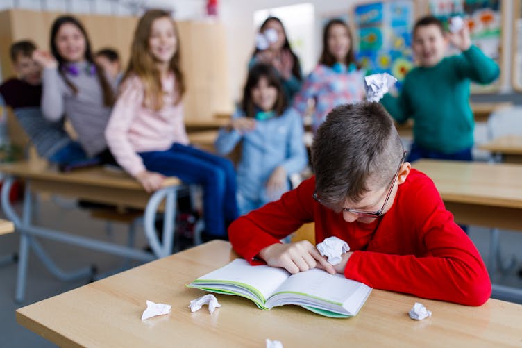 Des enfants jettent des boulettes de papier sur un enfant dans une classe. 
