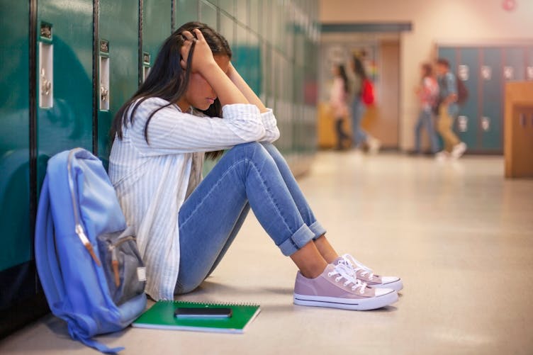 Une jeune fille est assise dans les couloirs d'une école la tête entre les bras. 