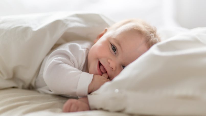 enfant dans lit souriant habillé en blanc