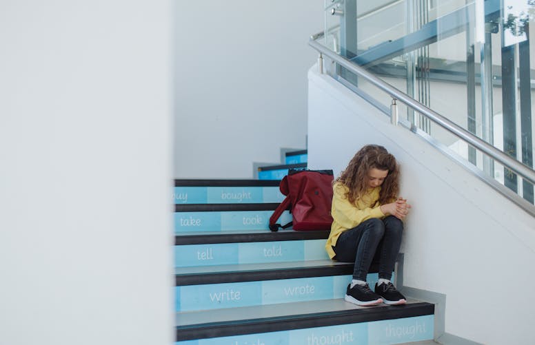 Une jeune fille est assise seule dans les escaliers d'une école. 