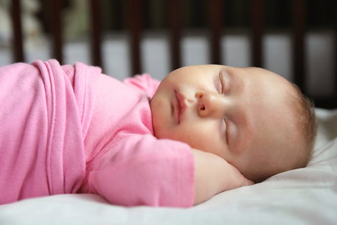 bébé dort allongé sur le dos dans body rose