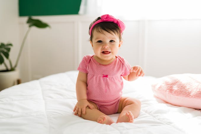 bébé fille tout de rose vêtue, assise sur un lit