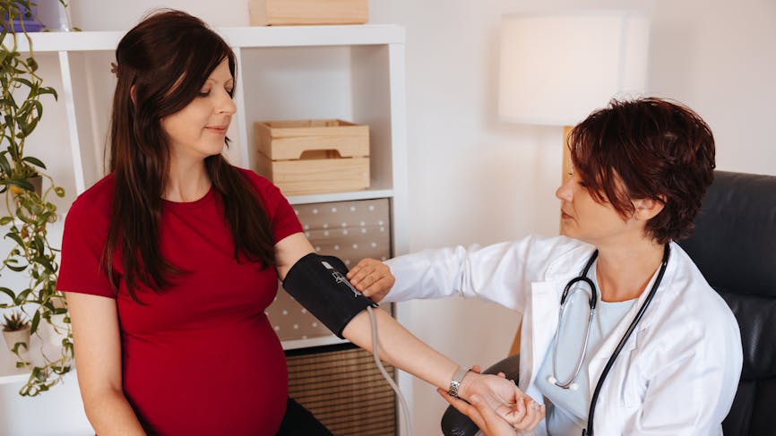 Une médecin prend la tension d'une jeune femme enceinte dans son cabinet