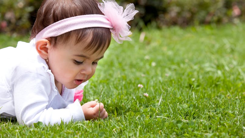 bébé allongé dans l'herbe bande rose dans les cheveux