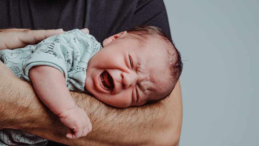 Un homme tient un bébé qui pleure sur son avant bras pour le réconforter