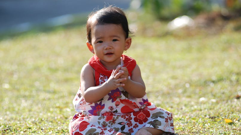 bébé fille assise dans l'herbe, robe a fleurs