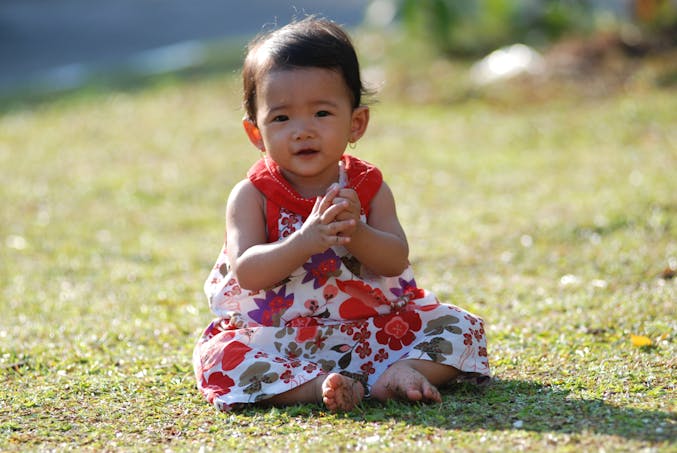 bébé fille assise dans l'herbe, robe a fleurs