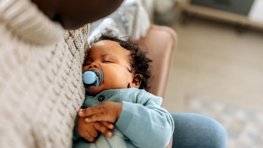 Un bébé dort avec sa tétine dans la bouche. 