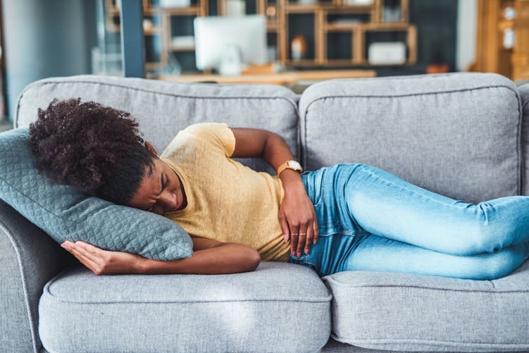 Une femme souffre de mal de ventre, sur son canapé.
