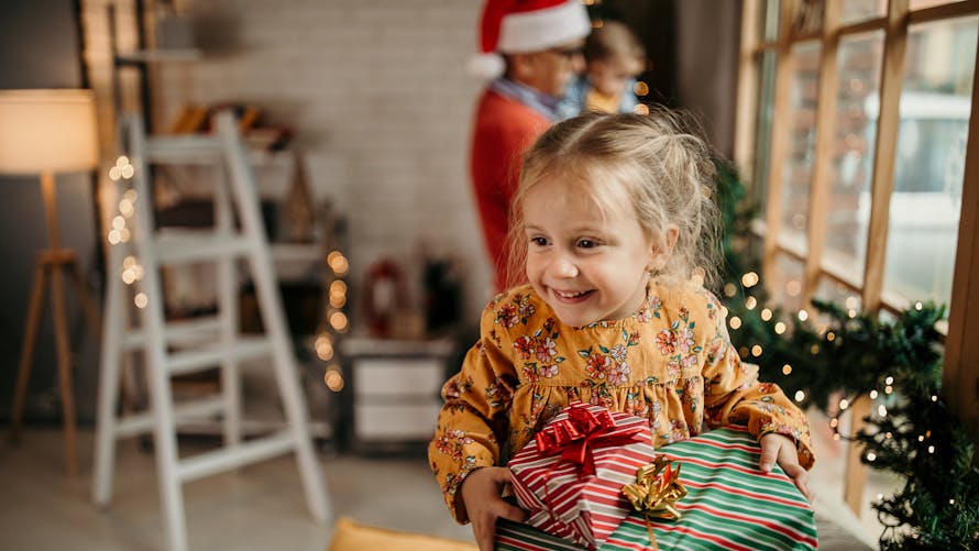 Une petite fille tient des cadeaux de Noël en souriant. 