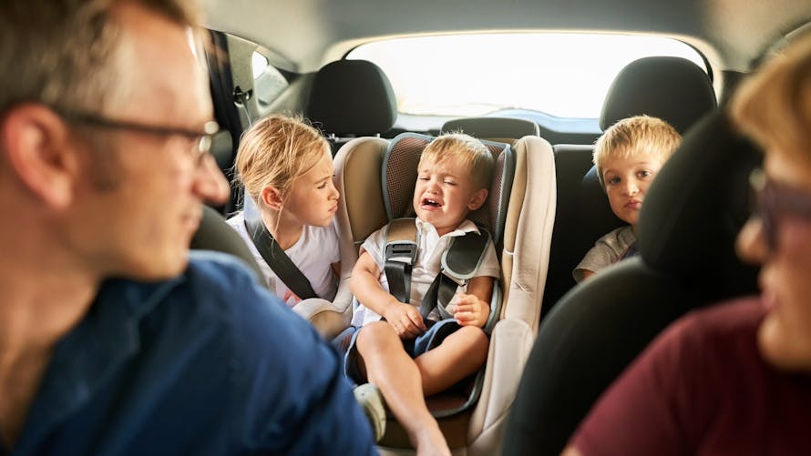 Une famille avec trois enfants à l'arrière d'une voiture, dont celui du milieu pleure. 