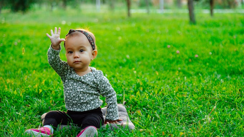 petite fille qui salue assise dans l'herbe