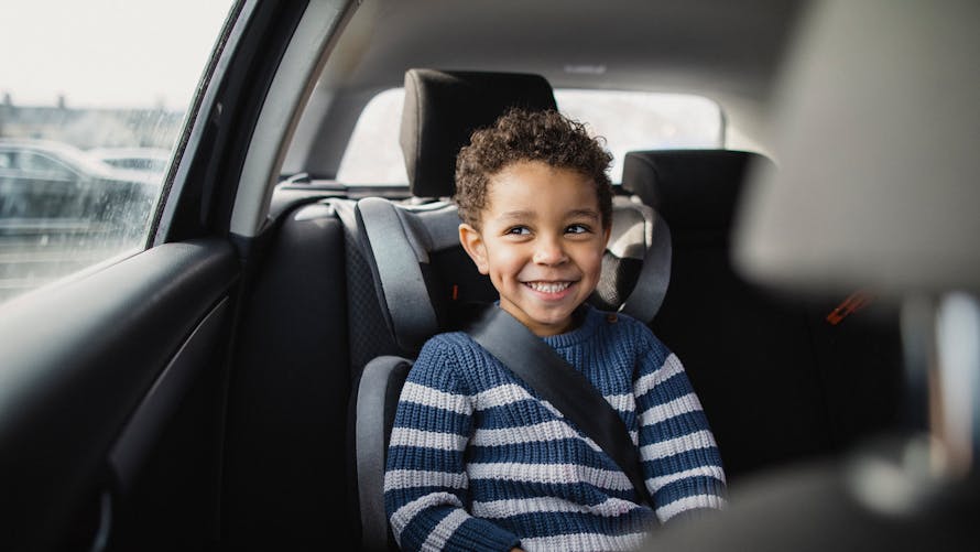 jeune garçon joyeux assis dans un réhausseur en voiture