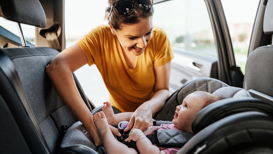 Une maman met son bébé dans un siège auto, dos à la route.