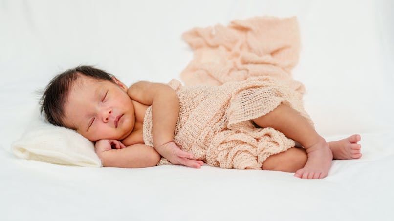 bébé fille qui dort dans couverture brodée rose