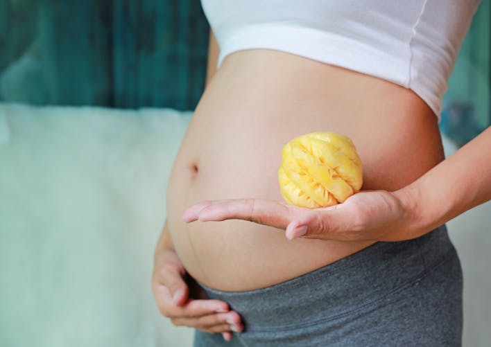 Une femme enceinte pose ventre arrondi avec un ananas épluché dans la main