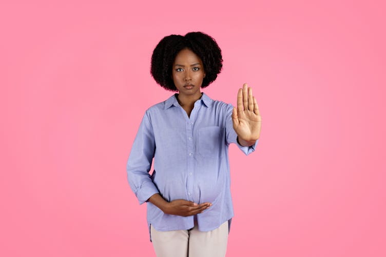 Une femme enceinte noire, une main sur son ventre, tend l'autre main en signe de refus "stop"