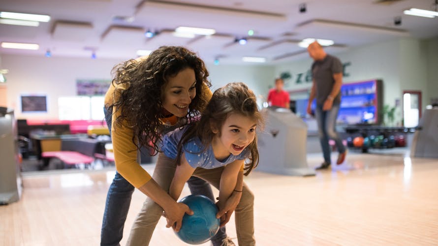 Une petite fille joue au bowling avec sa maman. 
