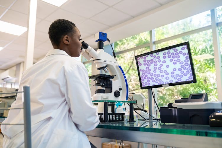 Une jeune femme noire aux cheveux cours fait de la recherche avec un microscope