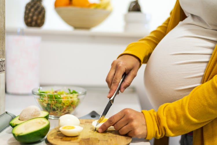 Une femme enceinte prépare son repas en coupant des oeufs durs