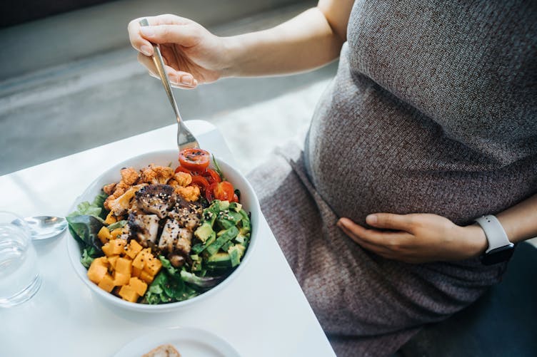 Attablée, une femme enceinte manger un bol végétarien à base de légumes et de tofu