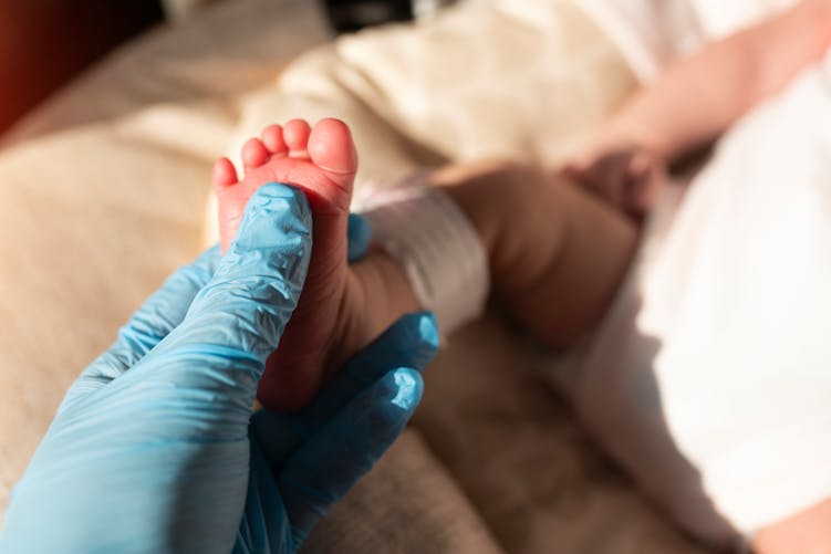 Une main gantée de soignant prend le pied d'un nouveau-né pour le test de guthrie dépistage néontala