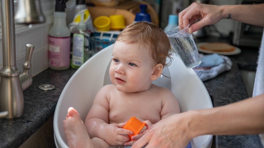 Un bébé se fait laver dans un lavabo.