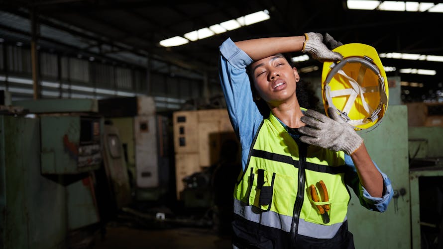 Une jeune femme travaillant dans un entrepôt avec un casque souffre de la chaleur