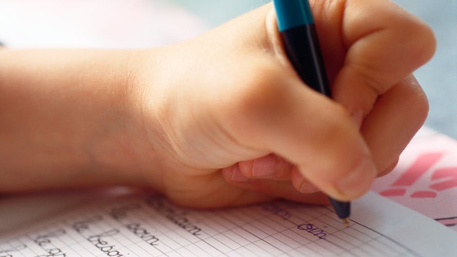 Un enfant écrit sur son cahier en tenant son stylo dans la main gauche