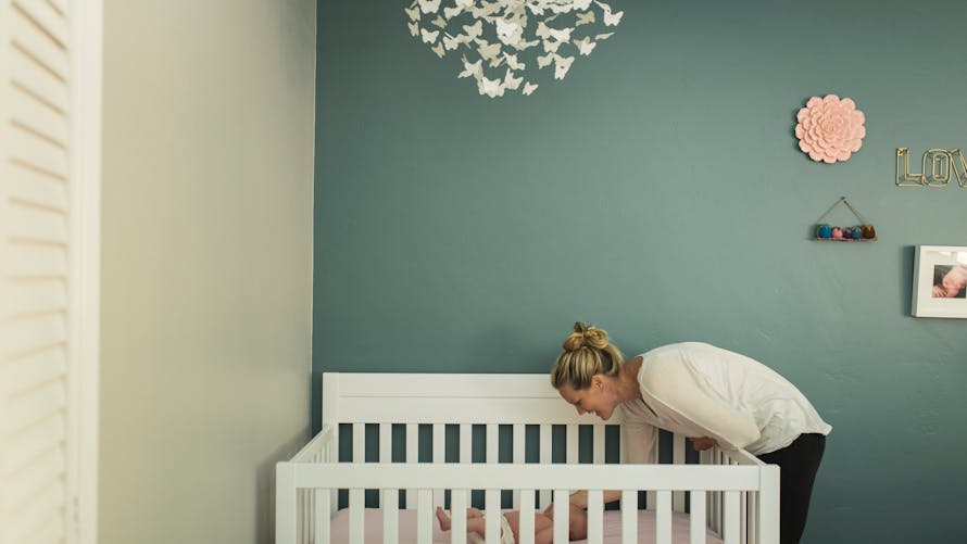 <p>Adulte se penchant sur un berceau dans une chambre d'enfant décorée.</p>