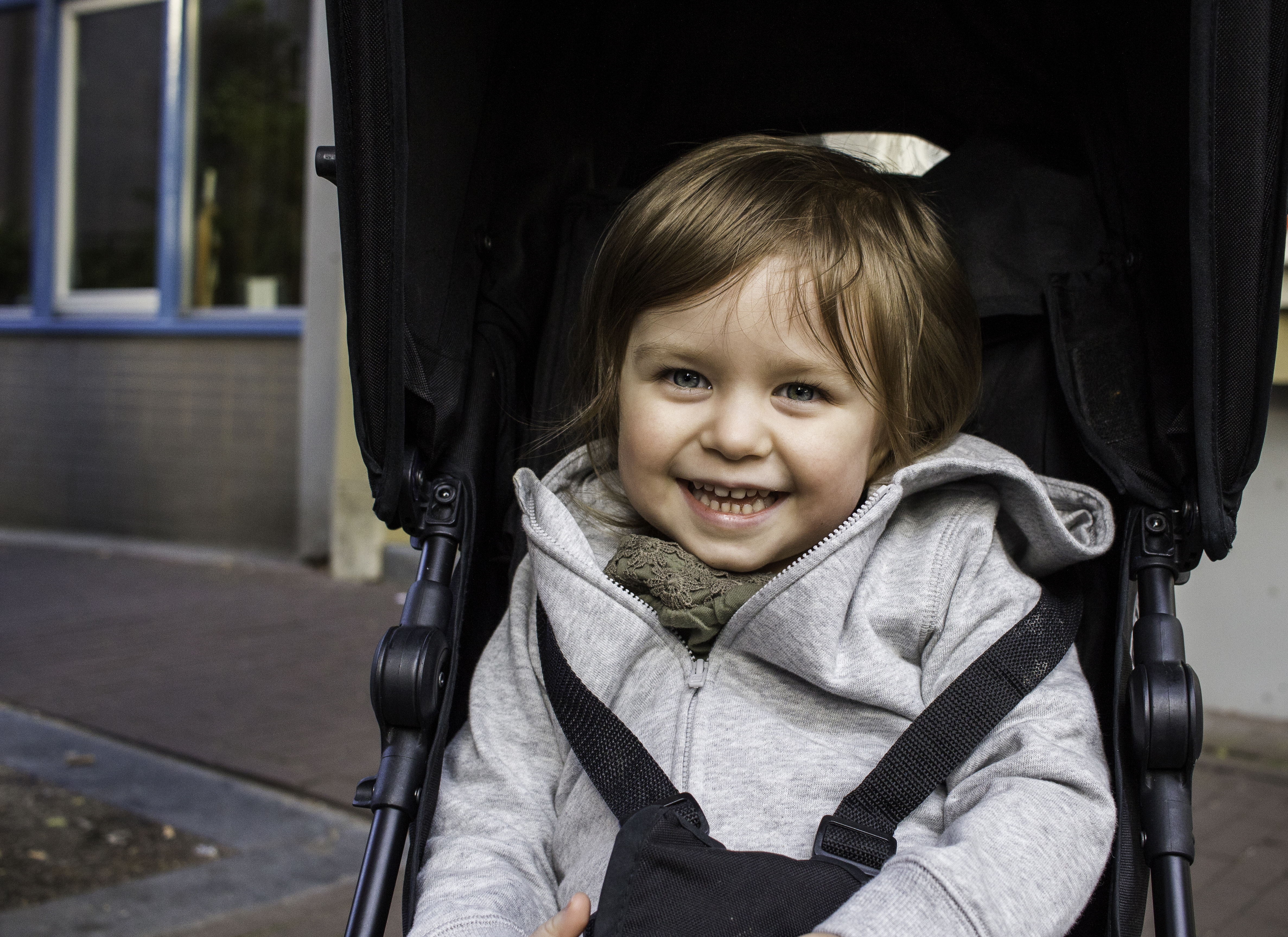 Enfant souriant assis dans une poussette noire, portant un manteau gris clair.