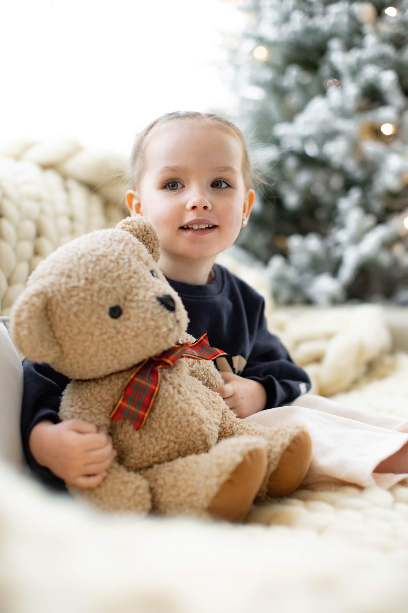 Petite fille tenant un ours en peluche dans ses bras, un sapin en arrière plan